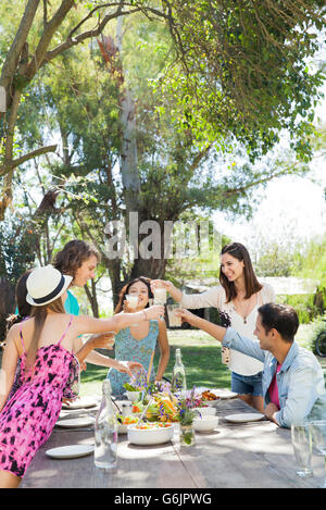 Friends having meal together outdoors, clinking glasses Stock Photo