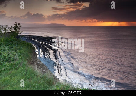 Setting sun shining through a heavy cloud with rays over the Bristol Channel, from the cliffs above Kilve Beach, Somerset Stock Photo