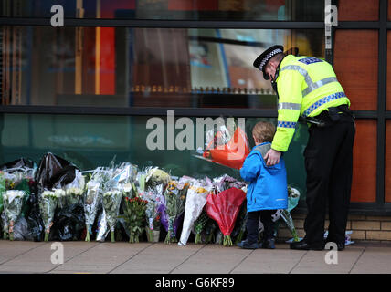 A police officer escorts a young boy as he leaves flowers near to the scene as emergency services remove wreckage to enable them to recover bodies from the Clutha Vaults pub in Stockwell Street close to Glasgow city centre continues, following the deaths of at least eight people - including the civilian pilot and two police officers of a police helicopter that crashed into the building on Friday evening.