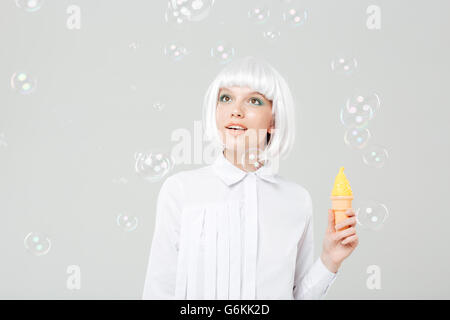 Happy cute young woman looking at soap bubbles and holding fake ice cream over white background Stock Photo