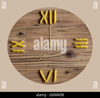 Penne pasta and spaghetti laid out on wooden background as a clock Stock Photo