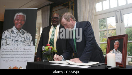 Taoiseach Enda Kenny signs a book of condolence for Nelson Mandela at the South African embassy in Dublin watched by Ambassador Azwindini Jeremiah Ndou. Stock Photo