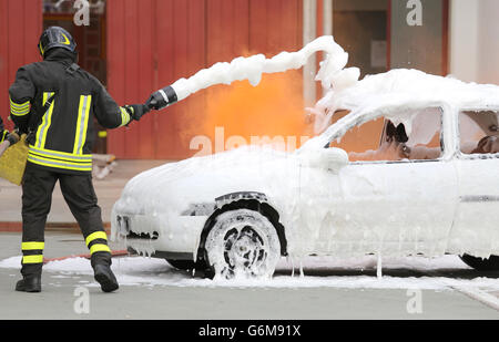firemen during exercise to extinguish a fire in a car with foam Stock Photo