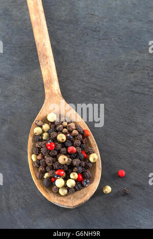 Coloured pepper on a wooden spoon isolated on slate Stock Photo