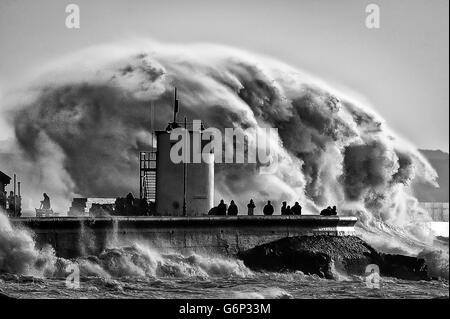 People watch and photograph enormous waves as they break on Porthcawl harbour, South Wales, where very strong winds and high seas create dangerous weather conditions. Stock Photo