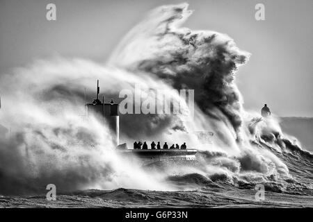 People watch and photograph enormous waves as they break on Porthcawl harbour, South Wales, where very strong winds and high seas create dangerous weather conditions. Stock Photo