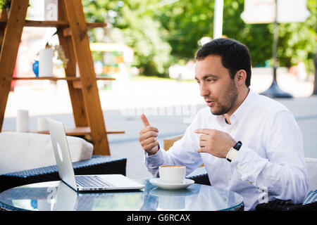 Closeup shot of young man smiling and using digital tablet at cafe. Guy is doing breakfast and making video call with laptop. Stock Photo