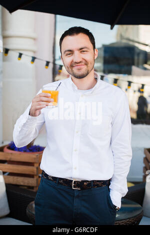 Handsome business man drinking fresh orange juice at outdoors cafe and smiling to the camera. Healthy lunch concept. Stock Photo