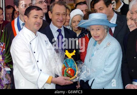 Queen Elizabeth II receives an early Easter gift, from a cafe chef during a walkabout in the city centre of Paris, after visiting Cafe Reflets on the Rue Montorgueil, which helps youngsters with their literacy and other skills. Hundreds of people lined the cobbled pavements of the street to see the Queen on the second day of her state visit. Well-wishers stood on their balconies waving as she walked down between the restaurants and shops. Stock Photo