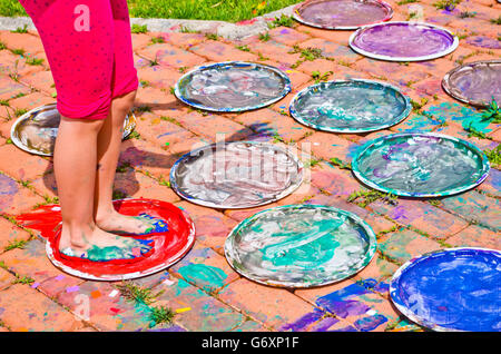 children playing making colorful designs with their feet immersed in the colorful tempera Stock Photo