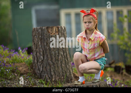 Little girl in a bad mood sitting near the house in the village. Stock Photo