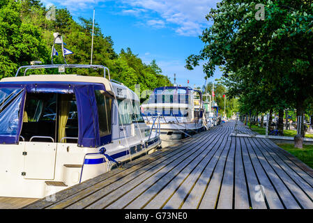 Soderkoping, Sweden - June 19, 2016: Moored motorboats at a wooden pier along the Gota canal. First boat is a Saga 315 powerboat Stock Photo