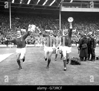 Manchester United players show the FA Cup to the 100,000 crowd as they carry it in a lap of honour around Wembley Stadium, London, after United had beaten Leicester City 3-1 in the Cup Final. The Cup is held by Maurice Setters (left) and the captain Noel Cantwell. On the right is Patrick Crerand. Stock Photo