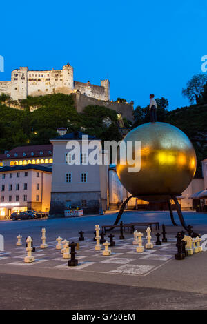 Night view of Kapitelplatz square with golden ball monument named Sphaera created by Stephan Balkenhol and Hohensalzburg Castle Stock Photo