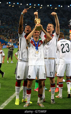 Germany's Thomas Muller celebrates on the pitch with the FIFA World Cup 2014 Trophy alongside teammates Per Mertesacker (right) and Jerome Boateng (left) Stock Photo