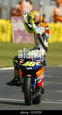 Italian Honda rider Valentino Rossi celebrates by sitting side saddle after crossing the line to win the MotoGP British Grand Prix at Donington, Leicestershire. Stock Photo