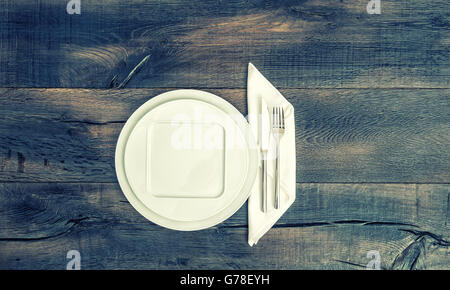 White plate, knife, fork and napkin. Empty diches on wooden background. Vintage style toned picture Stock Photo