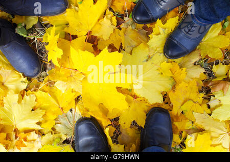 Top view of a foot in the autumn boots three people standing on the lawn covered with yellow fallen maple leaves Stock Photo