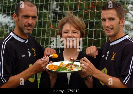 Norwich City Football Club Director Delia Smith is sandwiched between Norwich City players Adam Drury (right, Captain) and Craig Fleming (left, Club Captain) at the Norwich City training ground in Norwich. The celebrity chef and club shareholder shows off a plate of food that forms part of her Fuel Time Plan, a carbohydrate-rich, low-fat eating strategy for the team. Stock Photo