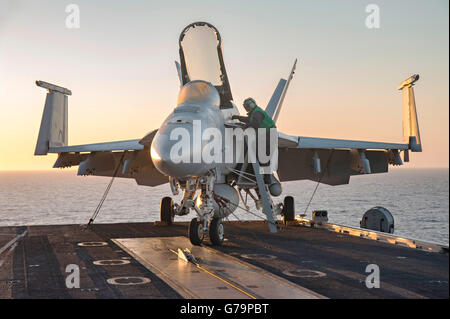 A US Navy Aviation Electronics Technician performs maintenance on an F/A-18E Super Hornet aircraft on the flight deck of the aircraft carrier USS Dwight D. Eisenhower at sunset June 14, 2016 in the Mediterranean Sea. Stock Photo