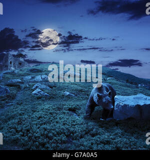 little brown bear walking among white sharp stones near the old castle on the hillside at night in moon light Stock Photo