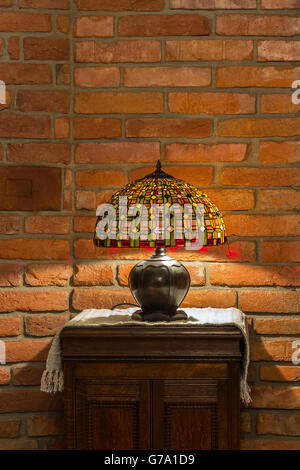 table lamp of stained-glass on old wooden stand on red brick wall background Stock Photo