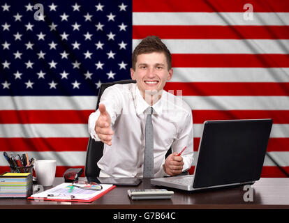 businessman sitting in office and reaches out on a USA flag on background Stock Photo