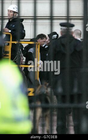 Fathers 4 Justice campaigner Jason Hatch dressed as Batman being led away by police on the ground at Buckingham Palace, London. The fathers' rights activist caused an embarrassing security breach at the royal residence when he managed to position himself on a ledge of the historic building despite the presence of armed police guards. After more than five hours standing on the ledge, Hatch was lowered to the ground with two police officers in a cherry picker. Stock Photo