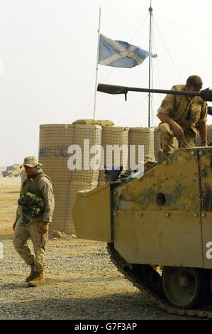 A soldier of the 1st Battalion Black Watch works on a warrior as an American solider walks past a Scottish Saltire flag that flies at half-mast in Camp Dogwood, after the suicide vehicles bomb which killed three Black Watch soldiers on Thursday. Stock Photo