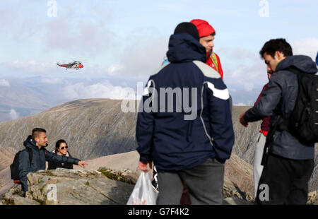 A Royal Navy rescue helicopter flies past hikers at the summit of Britain's tallest mountain, Ben Nevis, in the Lochaber area of the Scottish Highlands, Scotland. Stock Photo