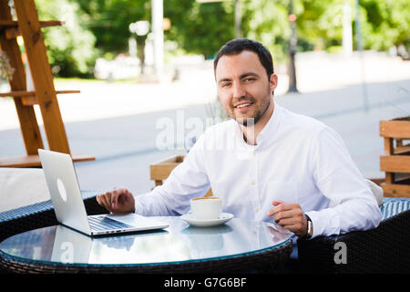 Handsome businessman working in a cafe on laptop, looking to the camera and smiling Stock Photo