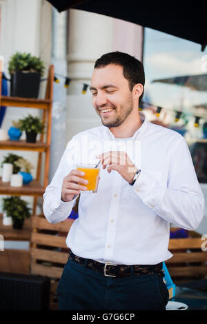 Handsome young Man Holding Glass Of Orange fresh Juice and smiling, Outdoors Stock Photo