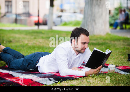 handsome young businessman reading book lying in the park Stock Photo