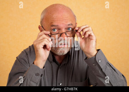 Elderly man, 59, putting on glasses, questioning look Stock Photo