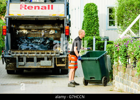 Soderkoping, Sweden - June 20, 2016: Male garbage collector rolling an empty trash bin back to a house in the neighborhood. Garb Stock Photo