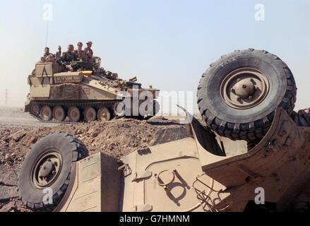 British soldiers riding on an armored personnel carrier pass a destroyed Iraqi APC in the desert following the liberation of Kuwait in Operation Desert Storm February 27, 1991 outside Kuwait City, Kuwait. Stock Photo