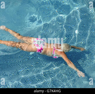 High angle view of aged woman that is swimming underwater in bright blue water of pool. Stock Photo