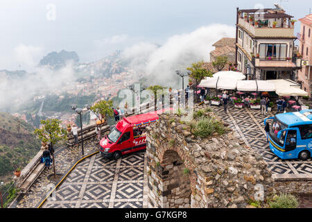 Panorama of Castelmola town square with tourists buses and an aerial view at Taormina covered with raining clouds at Sicily Stock Photo