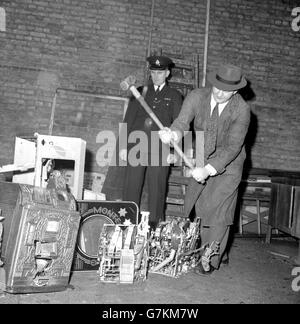 An engineer uses a sledge to destroy fruit machines ('one-armed bandits') and pin tables under the supervision of Inspector George Strachan at New Scotland Yard, London. Later on, they were burned. The machines were the first of 150 ordered to be destroyed after being seized by police in the last four months. Some of these machines were on show last week when the Metropolitan Police Commissioner explained the law relating to gaming machines, which comes into force on January 1st, 1961. Stock Photo