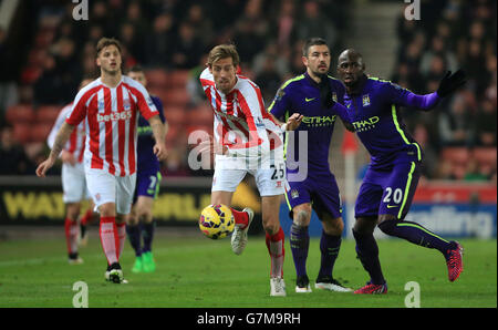 Stoke City's Peter Crouch holds off challenge from Manchester City's Aleksandar Kolarov (centre) and Manchester City's Eliaquim Mangala during the Barclays Premier League match at the Britannia Stadium, Stoke-On-Trent. Stock Photo