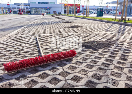 Urban space is swept with a wide red broom. Piles of dirt are lined up. Stock Photo