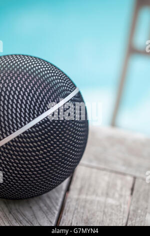 Detail of a ball-shaped loudspeaker on a wooden table with swimming pool at the background Stock Photo