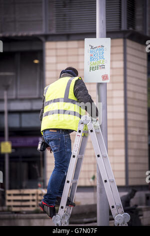 A man fixes a sign to a lamp post in Millennium Square in Bristol, as it is one of the two public spaces to go smokefree as a voluntary pilot is launched. Stock Photo