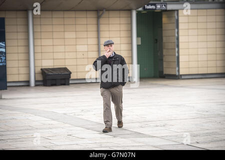 A man smokes a cigarette whilst walking through Millennium Square in Bristol, as it is one of the two public spaces to go smokefree as a voluntary pilot is launched. Stock Photo