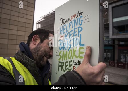 A man fixes a sign to a lamp post in Millennium Square in Bristol, as it is one of the two public spaces to go smokefree as a voluntary pilot is launched. Stock Photo