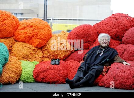 Artist Sheila Hicks, sits on her installation made from large-scale bundles of coloured fabric that visitors are welcome to sit on and interact with, during the preview at the Hayward Gallery, London, of 'Sheila Hicks: Foray into Chromatic Zones' exhibition. Stock Photo