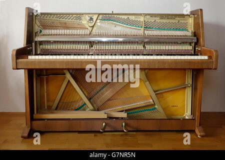 Dismantled upright piano stripped from front doors and fall showing inner mechanisms and strings. Stock Photo
