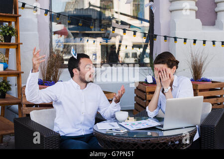 Businessmen shocked at colleague screaming and throwing papers in the air at outdoors cafe during lunch break Stock Photo