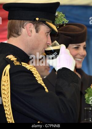 The Duke of Cambridge drinks a pint of Guinness as the Duchess of Cambridge looks on during their visit to Mons Barracks in Aldershot, Hampshire, as the Irish Guards regiment marks St Patrick's Day. Stock Photo