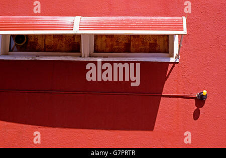 Side of building with yellow light bulb  and window shades against red building, street scene, urban scene Stock Photo